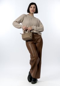 Beige ribbet striktrøje, brune faux læder brede bukser, sorte platform støvler og en lille beige håndtaske. Ensfarvet baggrund.