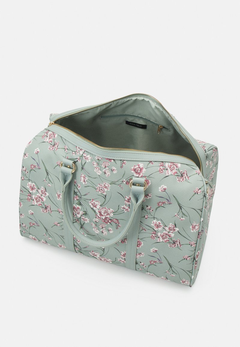 Sac de voyage floral en tissu vert menthe avec des fleurs roses. Doté de double poignées et d'une fermeture éclair dorée. Poche intérieure pour le rangement.
