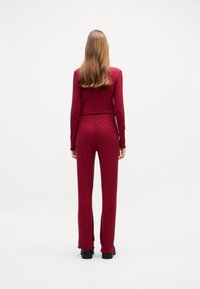 Top a maniche lunghe a quadri rossi abbinato a pantaloni attillati coordinati, con una sottile texture e orli smerlati, indossato con calzature nere spesse.