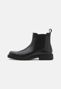 Bottines Chelsea en cuir noir avec des panneaux élastiques sur les côtés, un bout arrondi et un petit talon carré. Elles sont dotées d'une languette à l'arrière pour un enfilage plus facile.