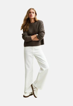 Bruine gebreide trui met gestructureerd patroon, cropped ontwerp; gecombineerd met witte wijde broek en witte sneakers met bruine accenten.