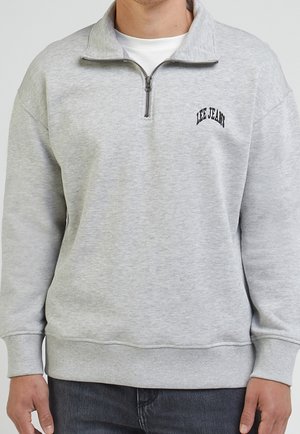 Sweat-shirt gris clair avec un col zippé mi-hauteur, des poignets et un ourlet côtelés. Présente un logo noir "LEE JEANS" sur la poitrine gauche. Matière en mélange de coton.