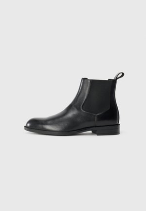 Black leather ankle boot with elastic side panels, rounded toe, and a pull tab. Smooth texture, flat sole, minimalistic design.