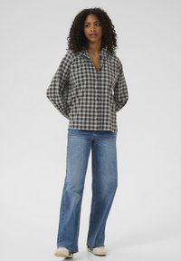Gray and white plaid button-up shirt with a collar, long sleeves, relaxed fit, paired with light blue flared jeans and beige shoes.