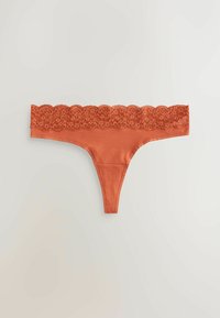 Culotte en tanga de couleur rouille avec une large ceinture en dentelle florale sur un fond clair et uni.