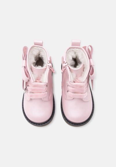 Paire de bottines roses pour tout-petits avec doublure blanche duveteuse, fermetures éclair latérales et nœuds décoratifs sur fond blanc.