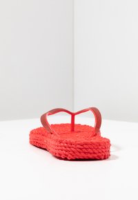 Punaiset flip-flop-sandaalit, joissa on teksturoitu punottu pohja ja kiiltävät remmit. Ominaisuuksina litteä muotoilu ja avokärkinen tyyli.