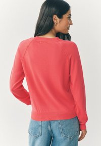 Korallfarbener Sweatshirt mit langen Ärmeln, ribbelten Bündchen und Saum; hat ein einfaches Design und eine glatte Textur. Kombiniert mit blauen Jeans.