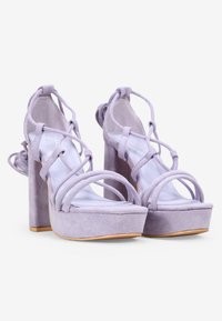 Sandalias de plataforma de ante lila con punta abierta, tacón alto y diseño de tiras entrelazadas. Presenta un detalle de lazo en la parte trasera y un forro interior suave.