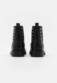 Černé kožené kotníkové boty se stříbrnými očky, oblé špičky a robustní podrážkou; poutko na zadní straně pro snadné obouvání.