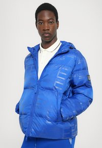 Chaqueta de plumas azul con acabado brillante, que presenta patrones grabados sutiles y una capucha desmontable. Incluye cremallera frontal y acentos de logotipo.