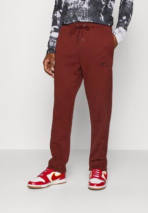 Nike joggers i dyb rød, med en elastisk talje og snøre samt sort "AIR" logo. Matcher med røde og hvide sneakers.