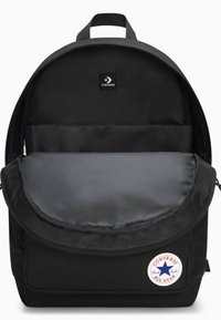 Mochila negra con un interior acolchado, que presenta una solapa horizontal gris. Incluye un parche bordado con el logo de Converse All Star.