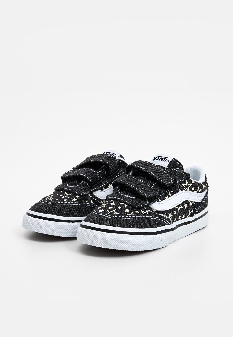 Zapatillas de lona negras con patrones de estrellas blancas, dos tiras de Velcro y una suela de goma blanca con una franja de acento negra.
