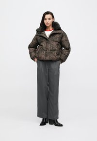 Gewatteerd jack met luipaardprint, kunstbontkraag, ritssluiting, voorzakken en een gestructureerde stof. Gecombineerd met grijze broek met wijde pijpen en zwarte laarzen.