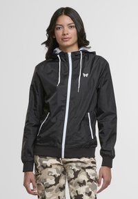 Black lightweight jacket with a silver zipper, white drawstrings, and a butterfly logo. Long sleeves with elastic cuffs, side pockets, and a hood.