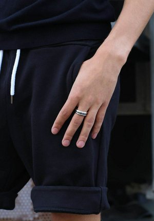 Zwarte sweatshorts met omgeslagen zomen, witte trekkoord en een hand die op de zak rust met een zilveren meerbandige ring.