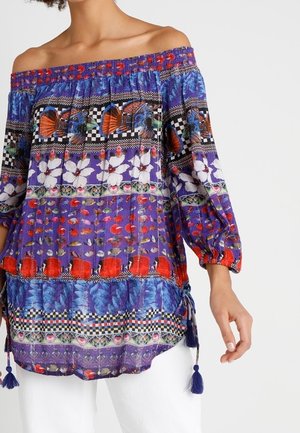 Off-shoulder lilla bluse med farverige blomster-, sommerfugl- og geometriske mønstre, 3/4-pufærmer og frynser i siderne.