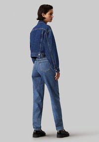 Chaqueta de mezclilla corta y jeans de cintura alta en diferentes tonos de azul. Presenta costuras clásicas, botones en la parte delantera y bolsillos laterales.