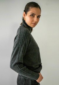 Pull à col roulé gris charbon, côtelé, avec des manches ajustées et un tissu texturé. Porté avec un jean foncé sur un fond clair.