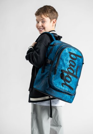 Modrý batoh s tie-dye vzorem a černými akcenty, s velkým nápisem. Obsahuje polstrované popruhy a více zipových přihrádek.