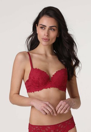 Reggiseno rosso in pizzo con coppe imbottite, bordi scallop e spalline regolabili. Presenta motivi floreali e una finitura liscia e strutturata.