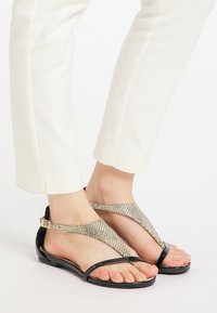 Sorte flade sandaler med T-stropdesing, der har metallic mesh-detaljer og en blank finish. Velegnet til afslappet brug.