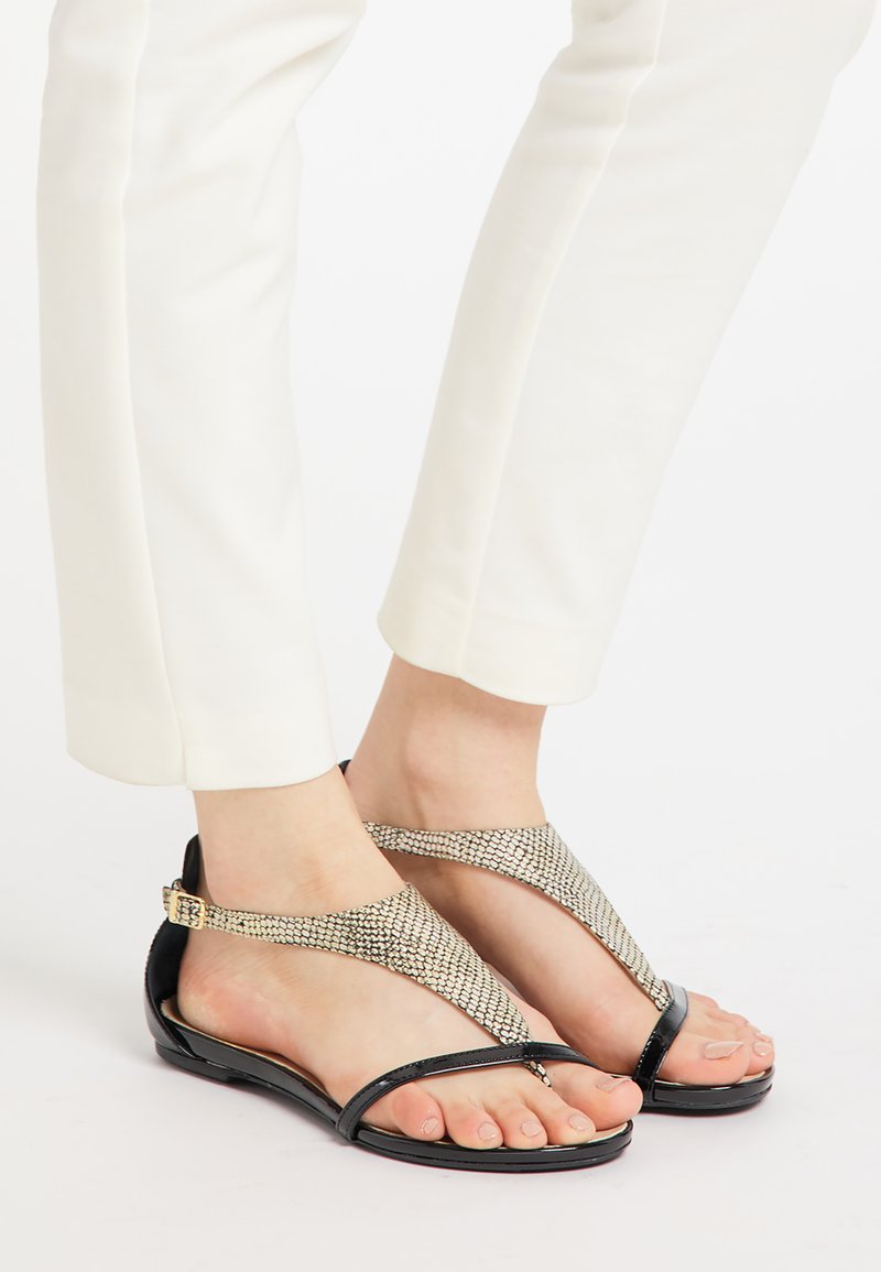 Sorte flade sandaler med T-stropdesing, der har metallic mesh-detaljer og en blank finish. Velegnet til afslappet brug.