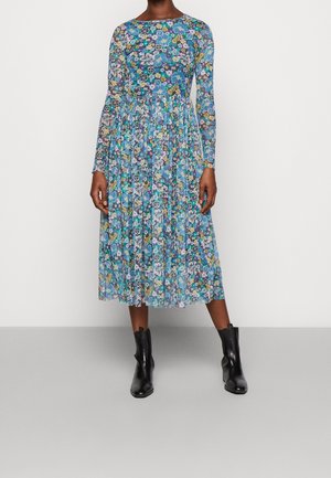 Vestido floral de manga larga en azul, con un corpiño ajustado, falda acampanada y tela transparente. Llevado con botas negras hasta el tobillo.