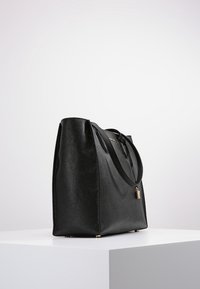 Sac cabas en cuir noir avec une finition texturée, équipé de poignées supérieures, de ferrures dorées et d'un petit détail de cadenas. Forme rectangulaire.