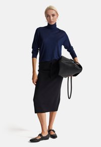 Maglione a collo alto blu navy, gonna a matita nera in maglia con orlo a costine, borsa nera con texture liscia e scarpe flat nere con dettagli a strappo.