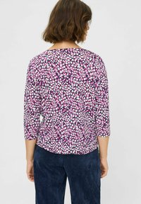 Purple floral blouse with three-quarter sleeves, featuring a scattered pattern of white and pink flowers on a dark background. Smooth fabric.