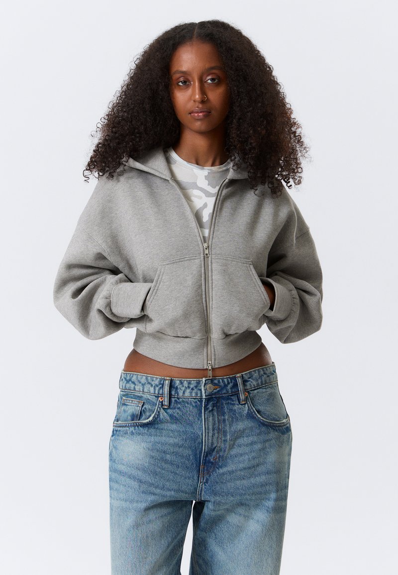 Γκρι cropped μπλούζα με φερμουάρ και μπροστινή τ σέπη, με ριμπ τελειώματα στις μανσέτες, συνδυασμένη με ανοιχτό μπλε τζιν παντελόνι με ξεβαμμένο σχέδιο και πέντε τσέπες.