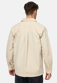 Beige, langærmet skjorte med en afslappet pasform. Har en knappet krave og manchetter, samt en rygstykke og plisserede detaljer for ekstra struktur.