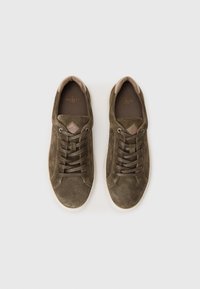 Baskets en daim vert olive avec bout arrondi, fermeture à lacets et accents beige clair sur la languette et le col. Semelle en caoutchouc.