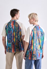 T-shirt med kortærmer og rund halsudskæring, prydet med et levende, flerfarvet abstrakt mønster på ryggen og kontrasterende ærmer i crèmefarve.