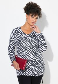 Svart och vit zebra mönstrad långärmad topp med V-ringning och paljetter, tillsammans med en röd läderclutch och svarta byxor.
