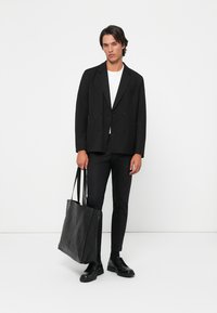 Blazer negro de corte cruzado sobre una camiseta blanca, combinado con pantalones negros ajustados, un bolso tote de cuero negro y zapatos negros.