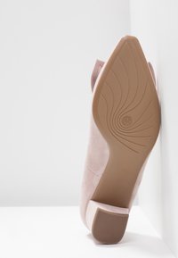 Chaussure à talon haute en suede rose, avec un bout arrondi, un talon effilé et une semelle en caoutchouc texturé présentant un motif en spirale.