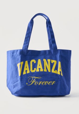 Μπλε τσάντα καμβά με κίτρινα γράμματα «VACANZA» με κεφαλαία και «Forever» με καλλιγραφικά στη μπροστινή πλευρά, με δύο ιμάντες για τον ώμο.