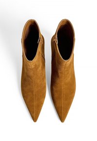 Bottes chevilles en suède marron avec un design à bout pointu et des zips sur le côté, présentant une texture lisse et une silhouette minimaliste.