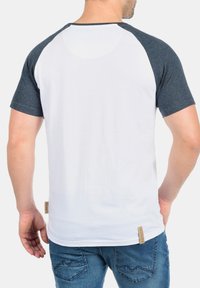 Raglan majica sivi rukavi i bijelo tijelo, izradjena od pamuka. Ima reljefnu oznaku na donjem lijevom dijelu.