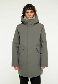 Grå vattentät parka med hög krage och stor huva, med sidfickor och rak silhuett. Slät textur, minimal design.