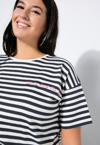 Černobíle pruhované tričko s krátkým rukávem, zdobené vyšitým růžovým textem na hrudi. Měkká bavlněná látka a volný střih.