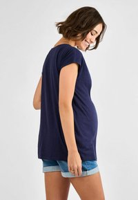 T-shirt premaman blu navy in tessuto morbido, maniche corte, vestibilità rilassata e orlo arrotondato. Abbinato a pantaloni shorts in denim arrotolati.