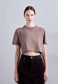 Smeđi skraćeni majica od mekog pamuka, s okruglim izrezom i kratkim rukavima. Uparen s tamnim kordura suknjom.