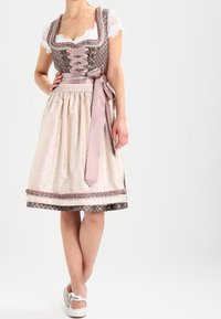 Tradycyjny dirndl z dopasowanym gorsetem w brązowym kolorze z koronkowym wykończeniem, różową satynową wstążką i kremową spódnicą z teksturowanym wzorem oraz akcentami na hemie.