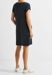 Laivansininen mekko, jossa on tummansiniset tekstuuriset paneelit takana, lyhyet hihat ja rento malli, yhdistetty valkoisiin tennareihin.