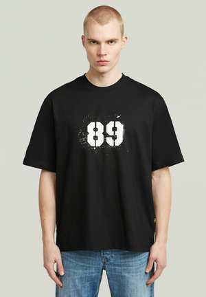 Zwarte katoenen t-shirt met een groot wit gesprayde nummer "89" op de voorkant, met een relaxte pasvorm en korte mouwen.