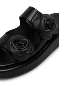 Black leather sandals feature two rose-shaped accents on the upper, with a flat sole and a minimalist design.